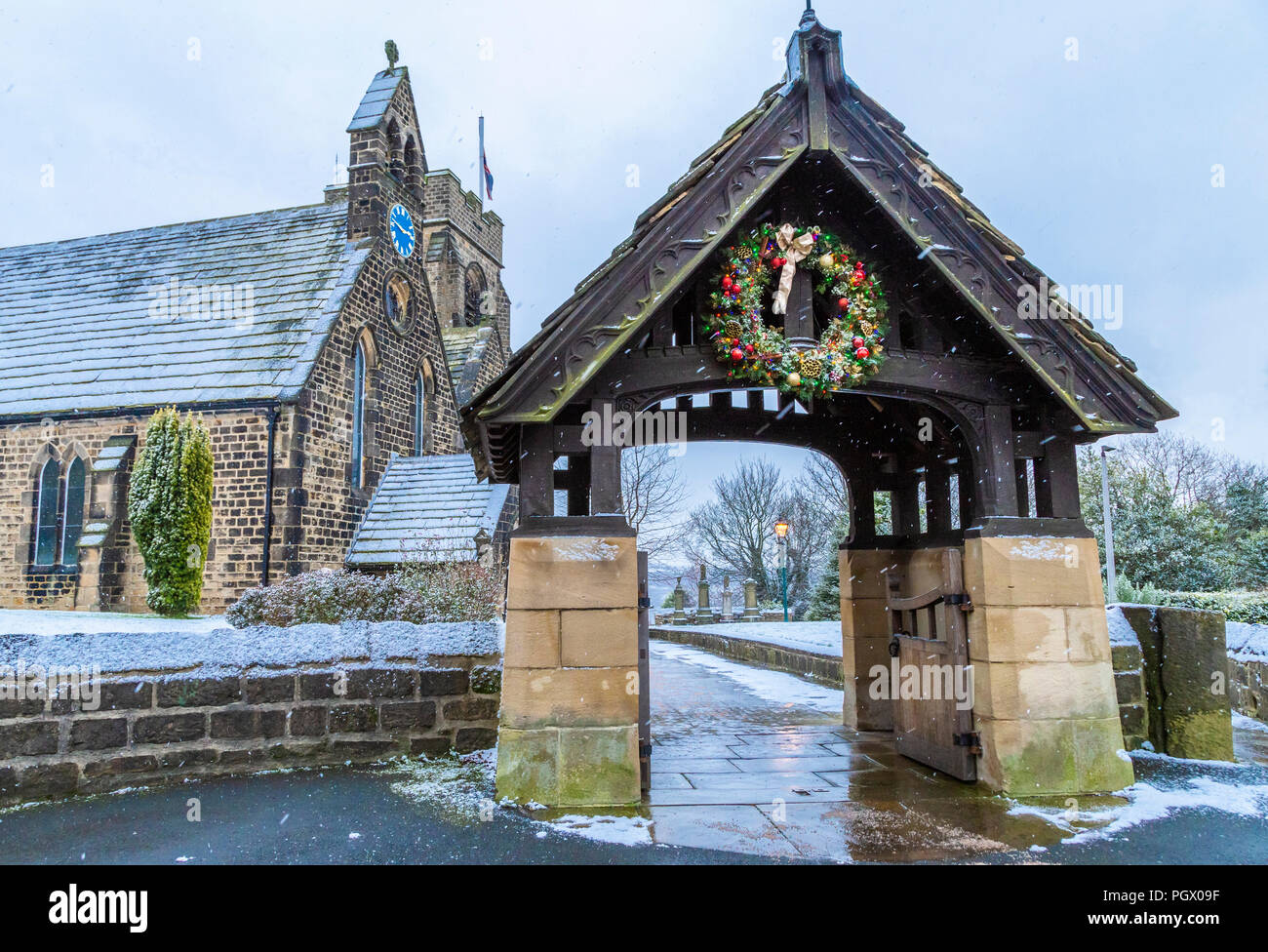 St John's Kirche, Baildon, Yorkshire, an Weihnachten. Eine dekorierte Kranz hängt über dem lychgate, das Foto wurde gemacht, als es schneite. Stockfoto