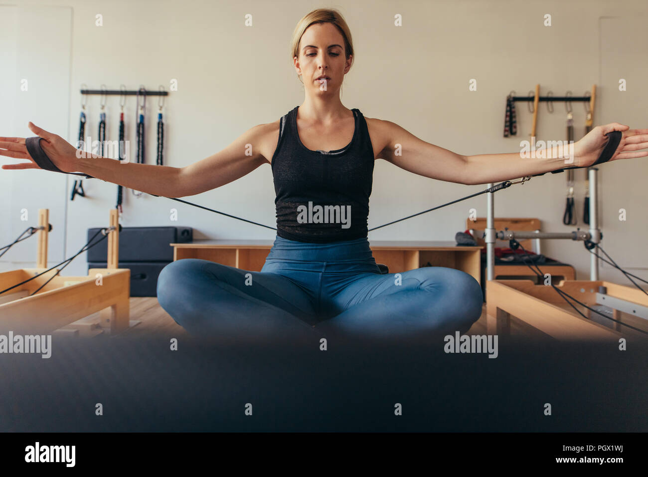 Frau sitzt auf einem Pilates Training Maschine ziehen Strech Bänder mit beiden Händen an der Turnhalle. Frau sitzt auf einem Pilates Trainingsgeräte mit Kreuz Stockfoto