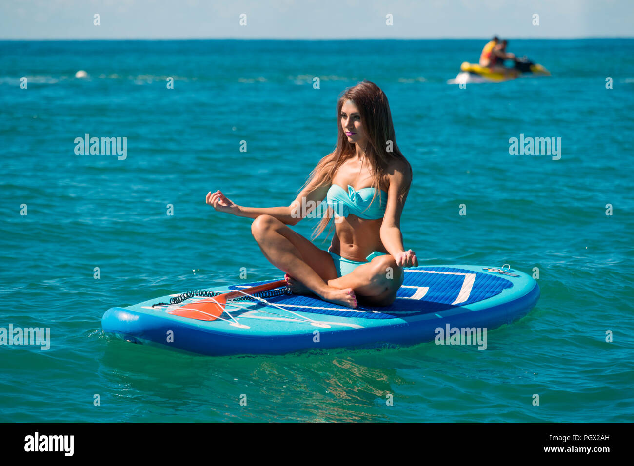 Frau entspannend auf einem SUP Verpflegung im Meer in einem Lotus darstellen. Paddle Board Yoga. Gesunder Lebensstil in Harmonie mit der Natur. Stockfoto