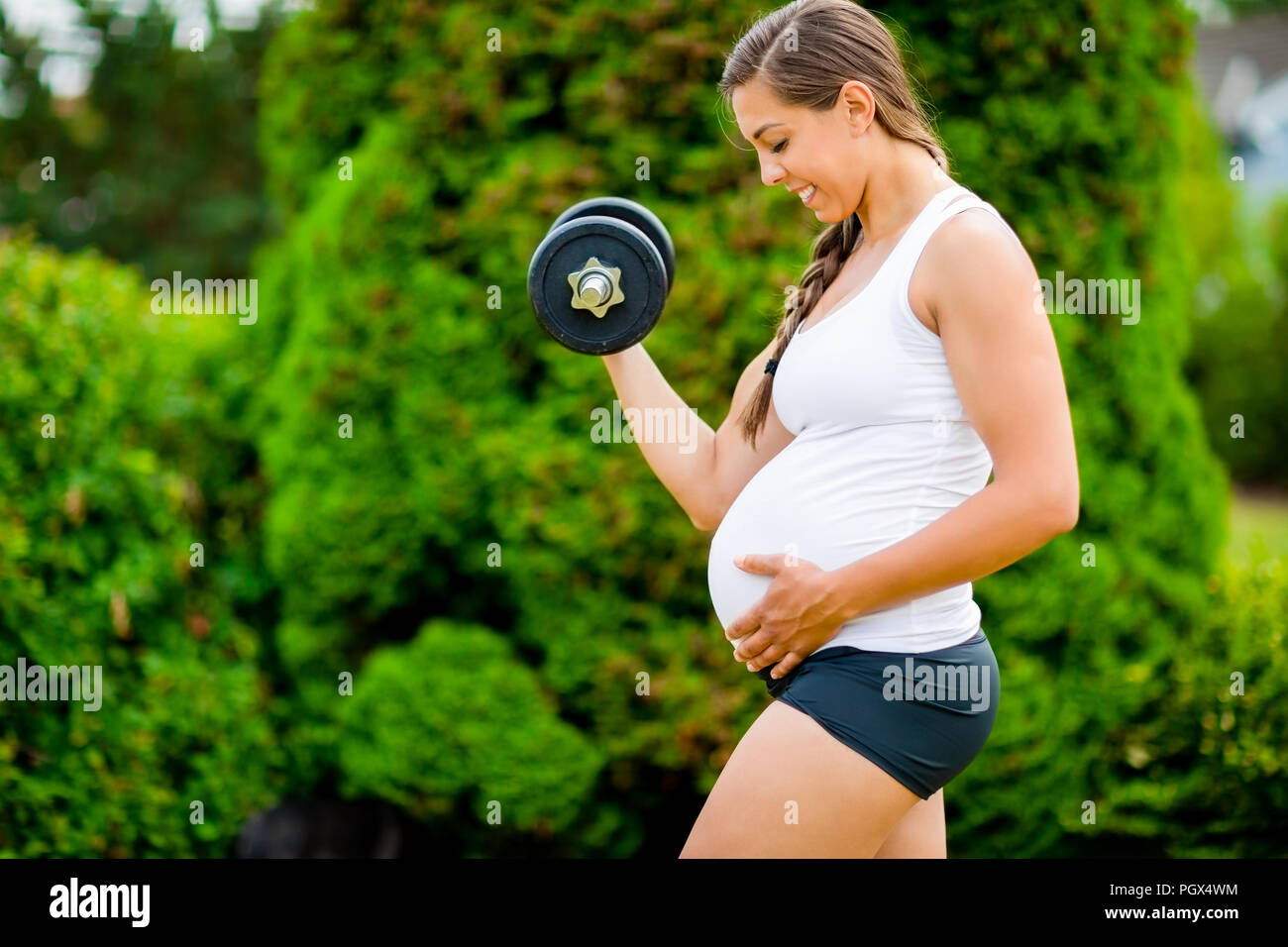 Die werdende Mutter Bauch berührt beim Anheben der Hantel in Park Stockfoto
