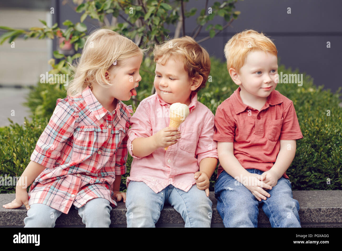 Group Portrait von drei weißen Kaukasischen cute adorable lustig Kinder Kleinkinder sitzen zusammen Eis-creme Essen. Liebe Freundschaft Eifersucht anhand von quantitativen Simulatio Stockfoto