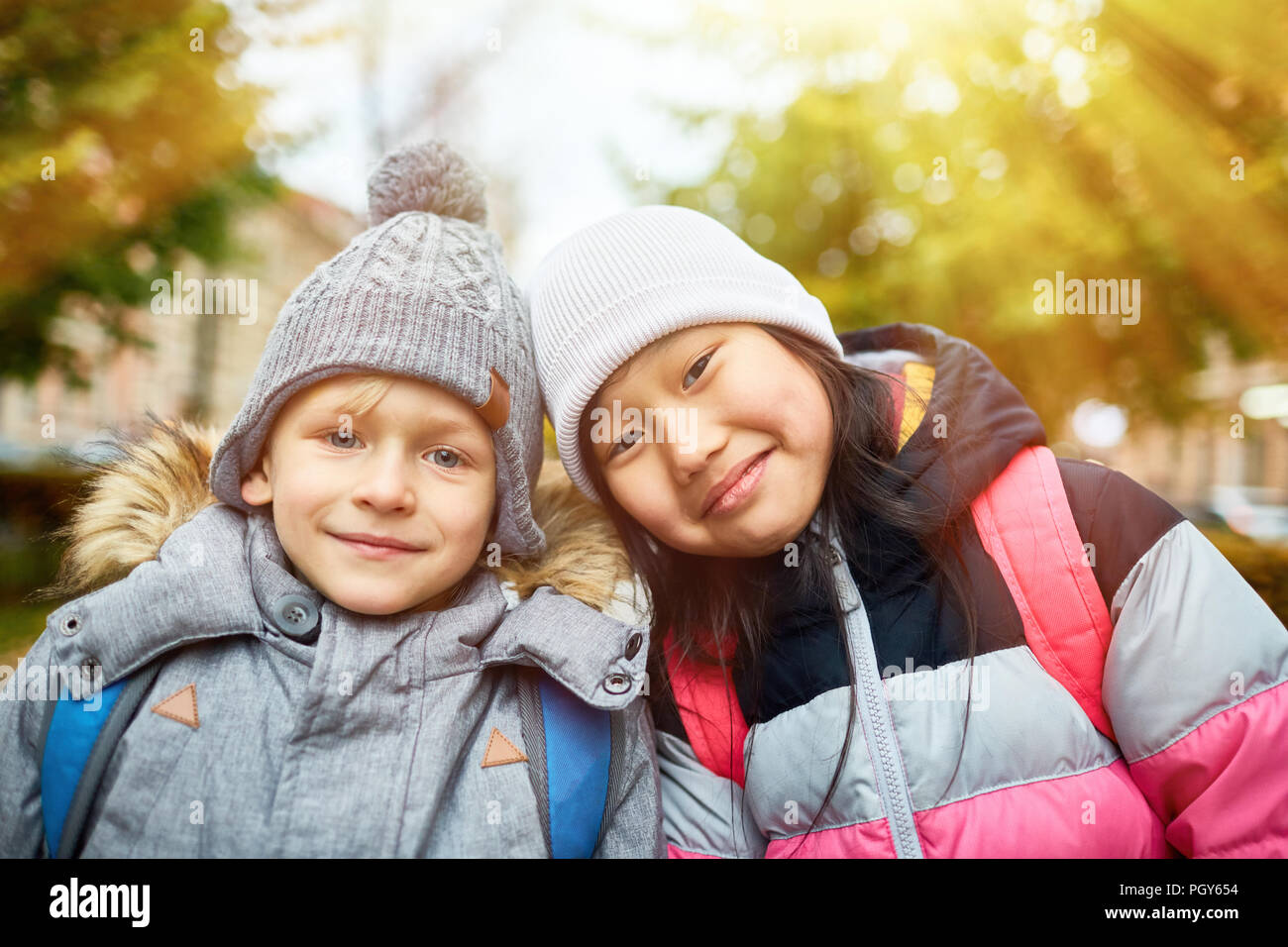 Cute interkulturelle Kinder in warmen Jacken und Mützen, die sie in der städtischen Umwelt Stockfoto