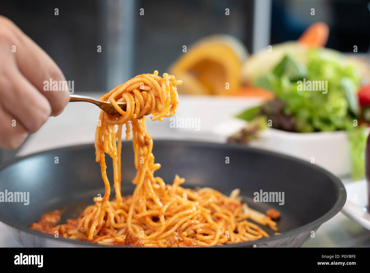 Spaghetti aufgehoben durch Gabelstapler mit Gemüse und Salat Teller Hintergrund. Essen und Cousine Konzept. Italienisches Essen in der Küche Thema. Rezept und Menü Thema. Stockfoto