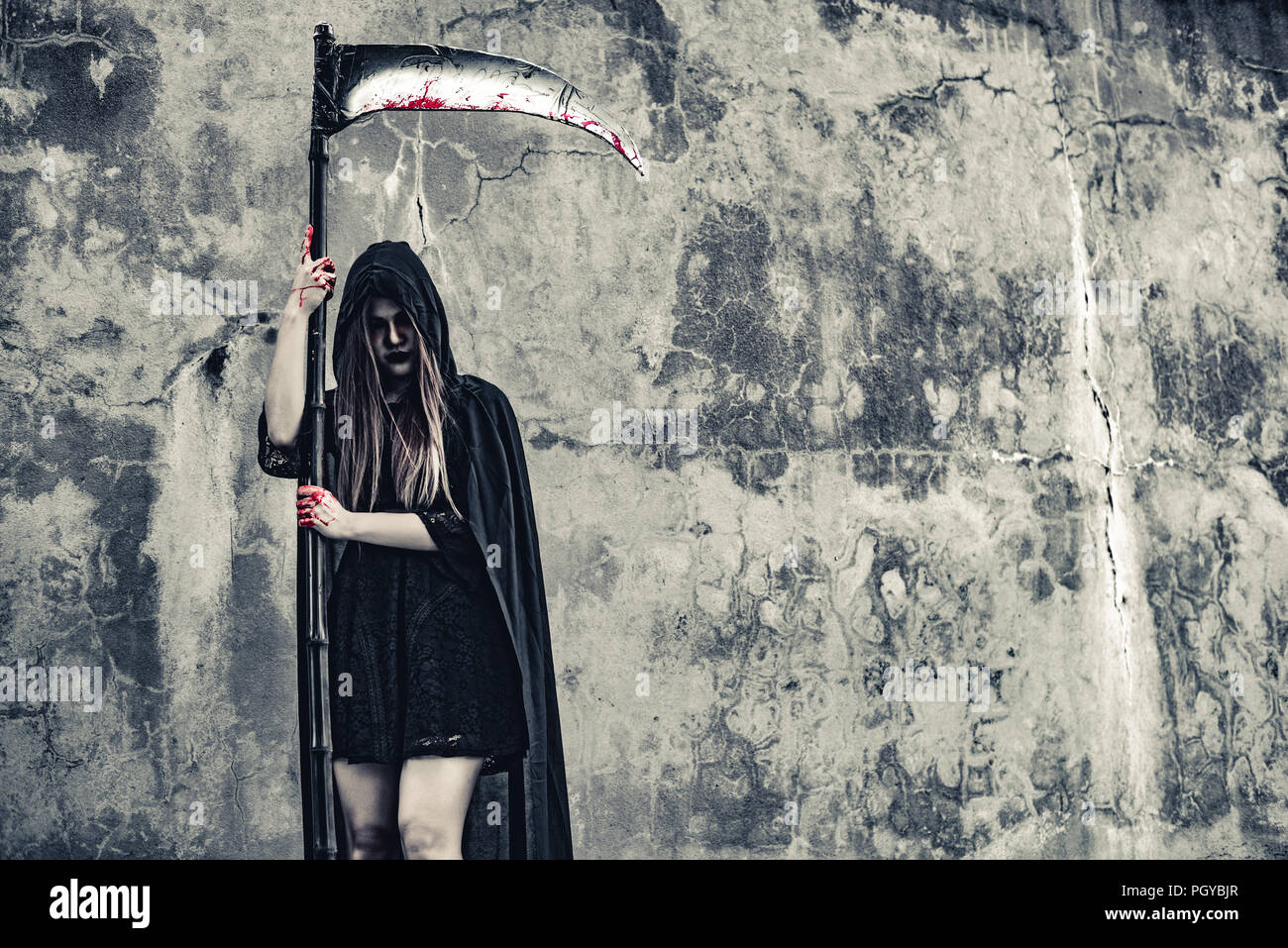 Daemon Hexe mit Reaper stand vor der grunge Wand Hintergrund. Halloween und religiöses Konzept. Daemon Engel und Satan Thema. Stockfoto