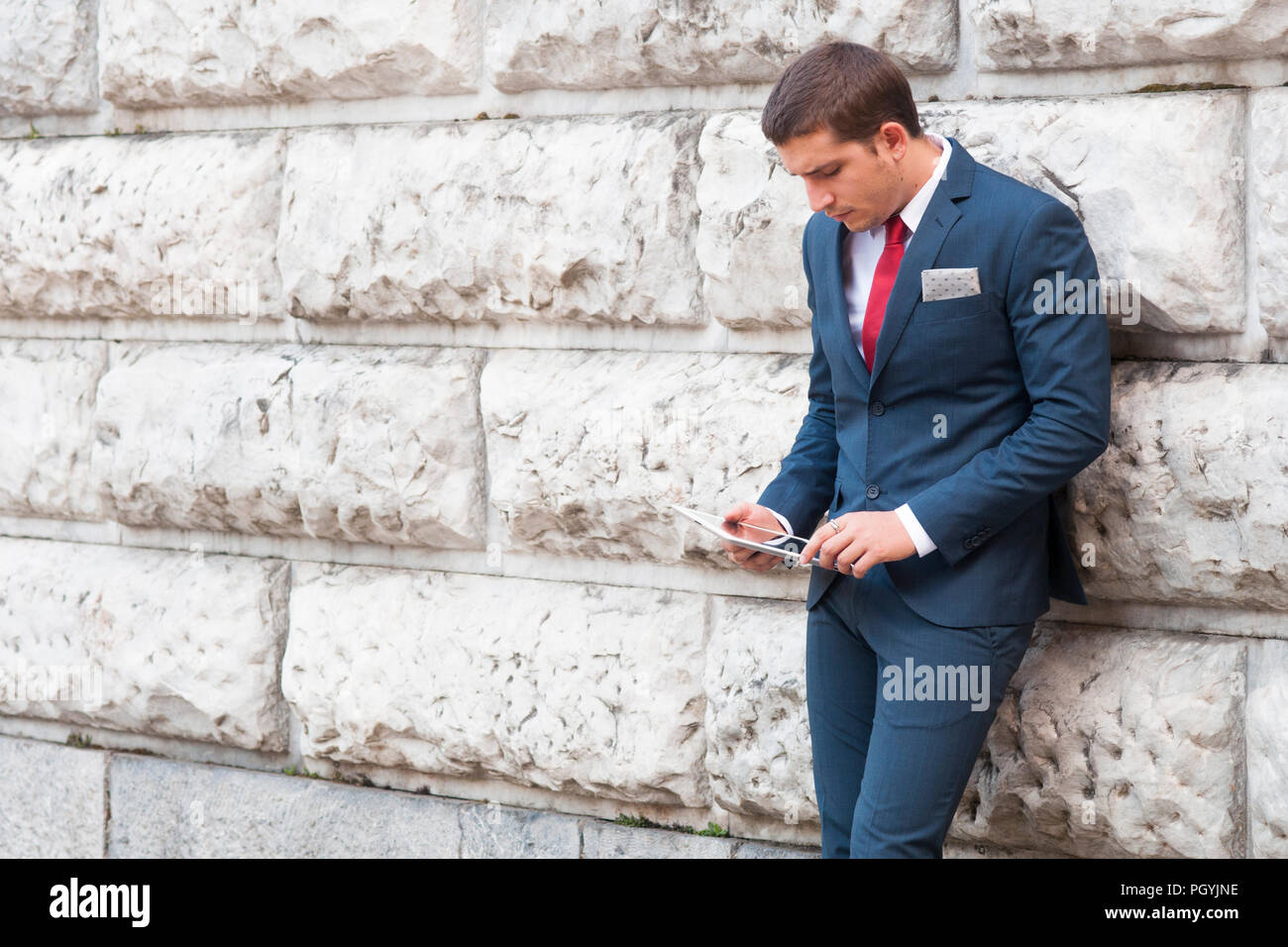 Junge gut aussehender Geschäftsmann in Anzug und Krawatte Lesen von Tablette gegen eine Wand aus Marmor Stockfoto