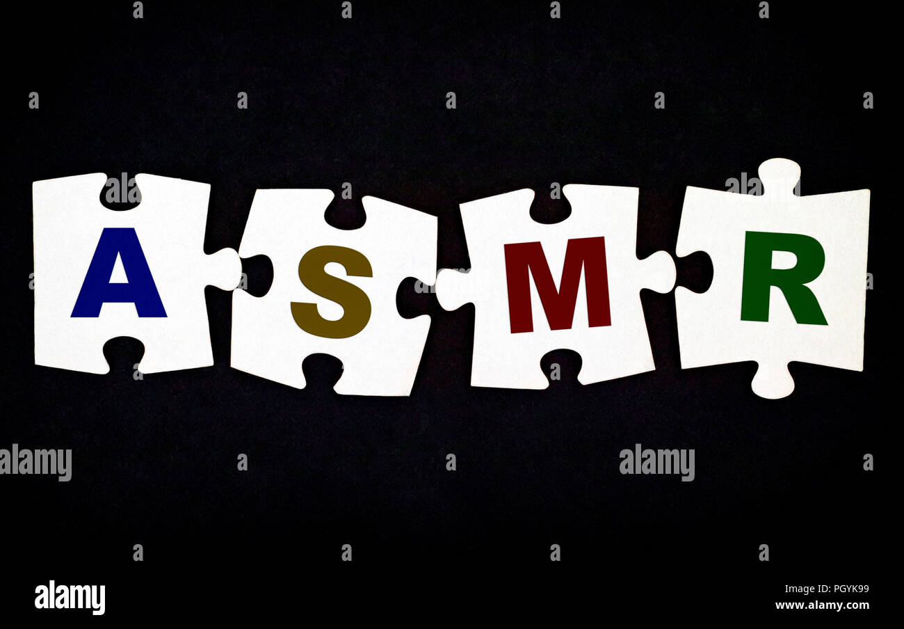 Vier Stücke von Puzzle mit Buchstaben ASMR auf schwarzem Hintergrund. Close-up. Stockfoto