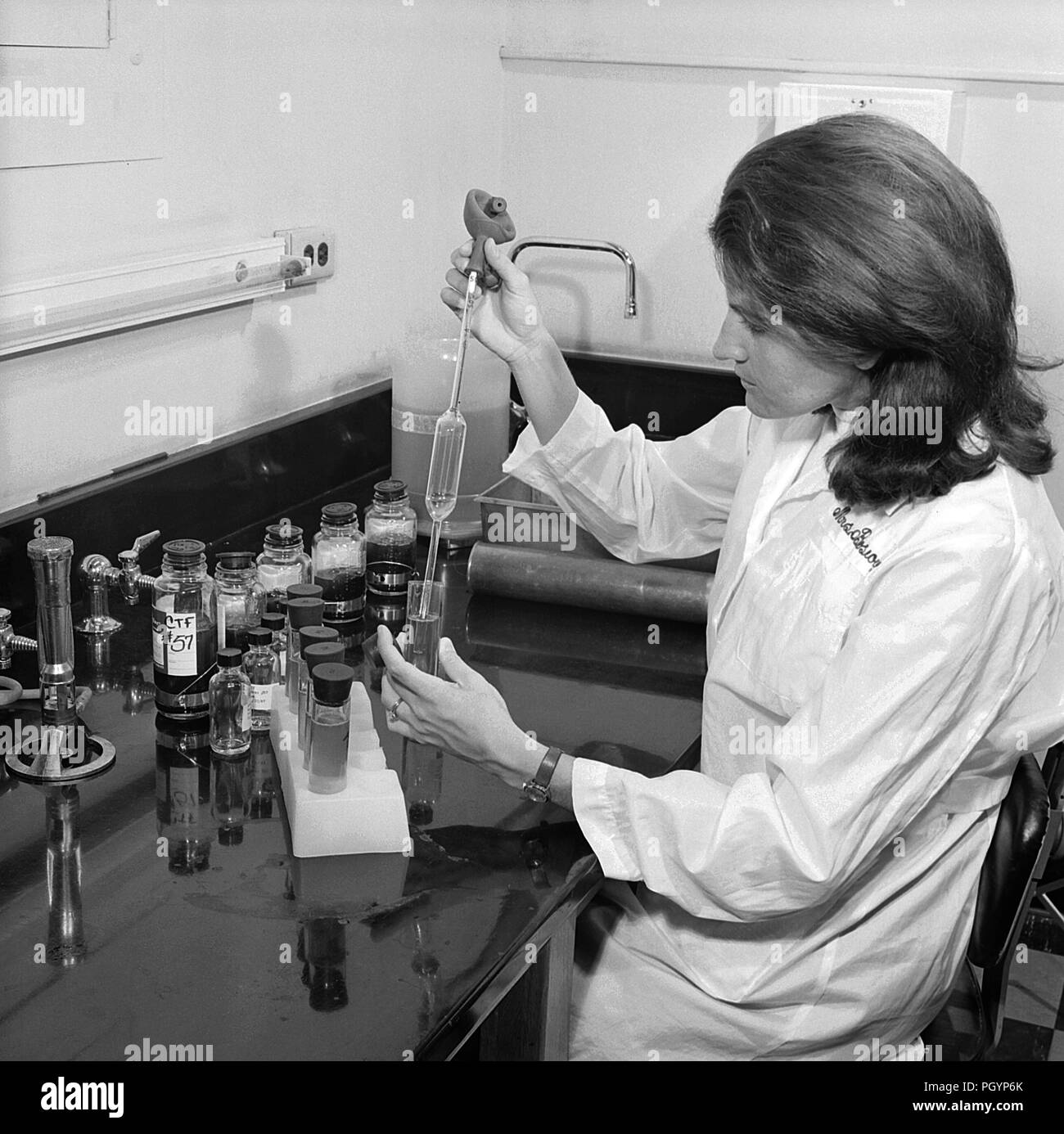 Schwarz-weiß Foto eines weiblichen Labortechniker, trägt einen weissen Mantel während der Verarbeitung einer Charge der Immune Sera, aka Antiserum, mit Fläschchen und andere wissenschaftliche Apparat auf dem Schreibtisch vor ihr sichtbar, mit freundlicher CDC / Dr. Andreas Fodor, 1967. () Stockfoto