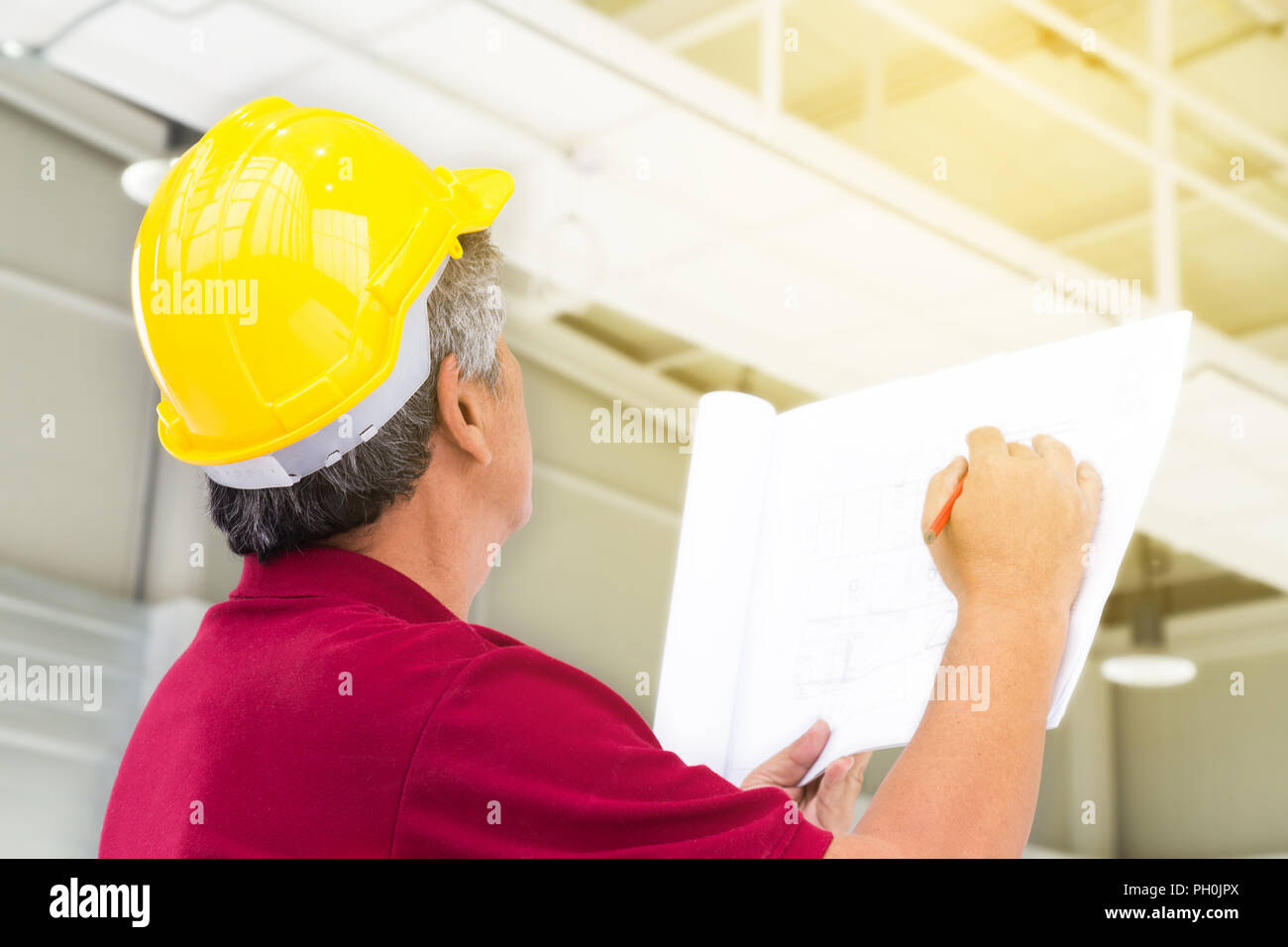 Asiatische Ingenieur in Gelb hart Schutzhelm ist Überprüfung der Struktur des Gebäudes und der Blaupause der Fabrik in der Fabrik Baustelle mit Sunbeam. Stockfoto