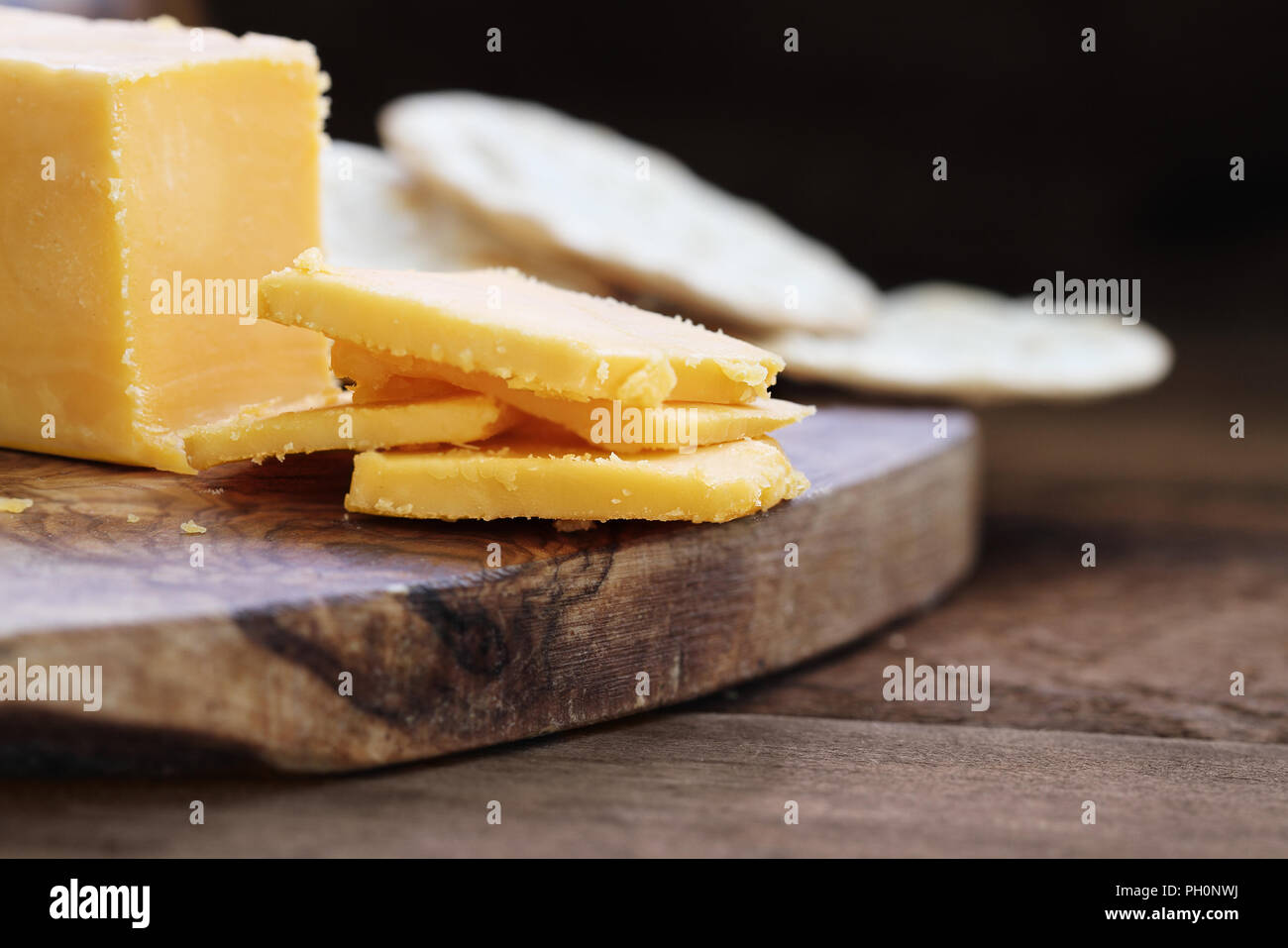 Block von Cheddar Käse und Scheiben über eine rustikale Hintergrund.. Extrem flache Tiefenschärfe mit selektiven Fokus auf Käse. Wasser Cracker in der Bac Stockfoto