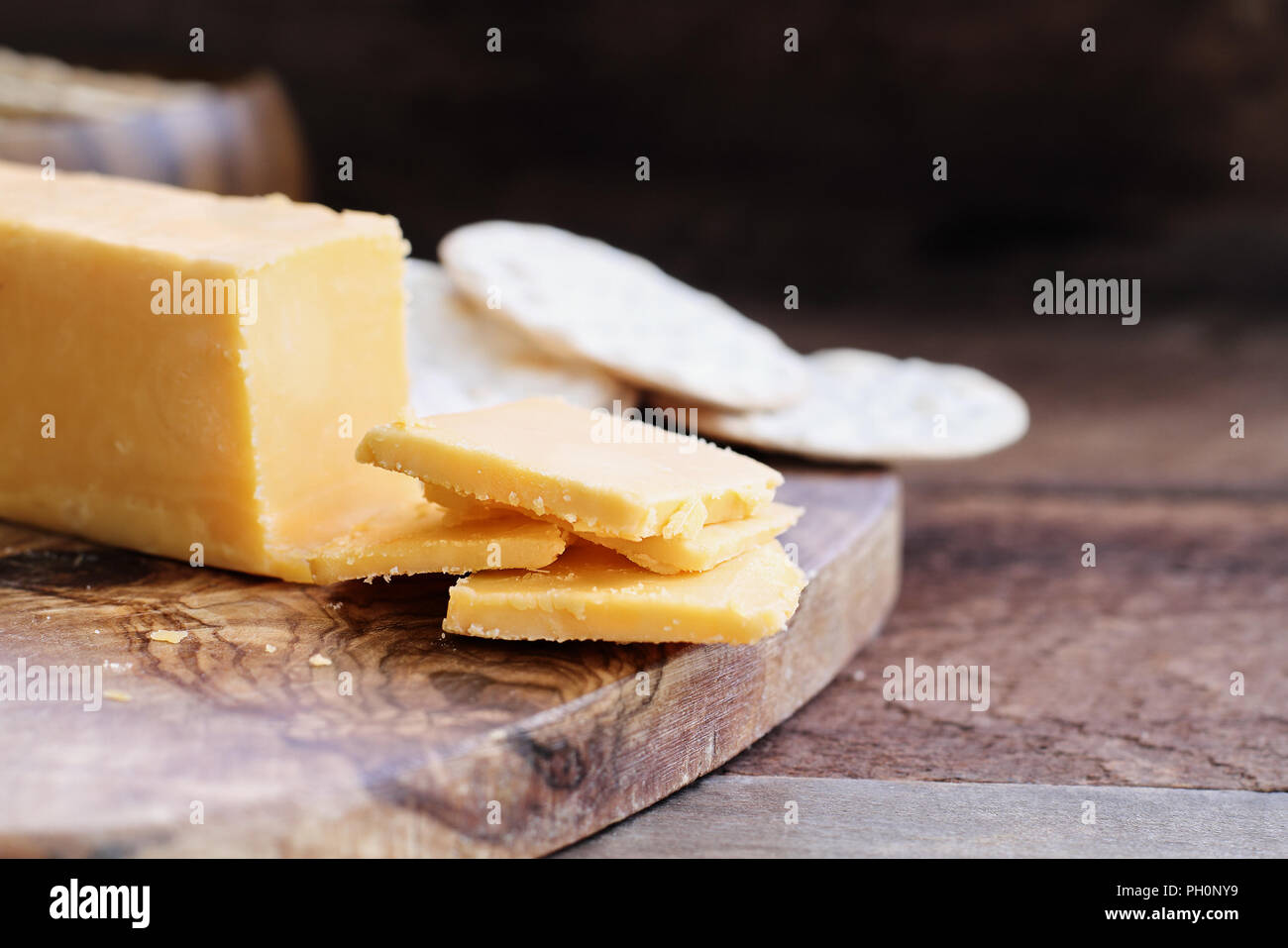 Block von Cheddar Käse und Scheiben über eine rustikale Hintergrund.. Extrem flache Tiefenschärfe mit selektiven Fokus auf Käse. Wasser Cracker in der Bac Stockfoto