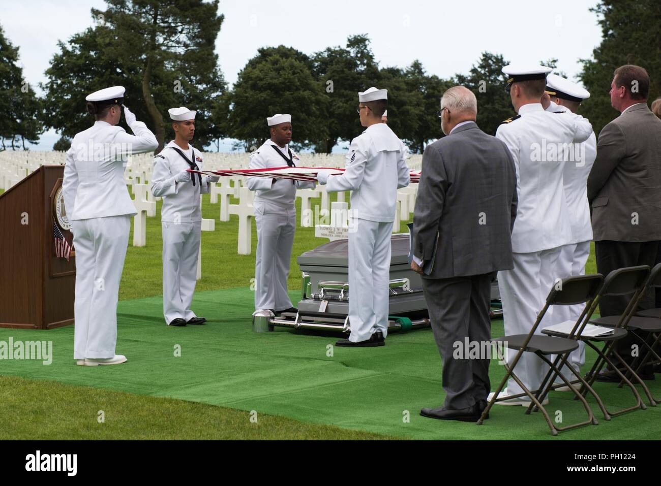 Normandie, Frankreich (19. Juni 2018) Die U.S. Naval Hospital Neapel Ehrengarde hält die amerikanische Flagge über die Überreste von Radioman 2. Klasse Julius "Henry" Pieper als "Hähne" wird während einer Trauerfeier in der Normandie amerikanische Friedhof gespielt. Henry Pieper und seinem Zwillingsbruder, Radioman 2. Klasse Ludwig "Louie" Pieper, waren beide getötet, als ihr Schiff, Landing Ship Tank (LST) 523, schlug eine vor der Küste von Frankreich am 19. Juni 1944. Louie's Überreste wurden sofort gefunden, aber Henry's Überreste wurden nicht bis Dezember 2017 identifiziert. Die Familie beantragt, dass Henry in der Normandie n begraben werden. Stockfoto