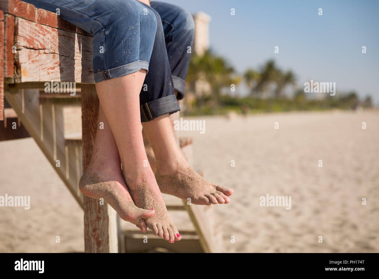 Nahaufnahme des Mannes und der Frau die Füße. Leute sitzen auf der Holzterrasse am Strand. Paar beim Sommer Tag am Strand. Ferienhäuser Stimmung. Stockfoto