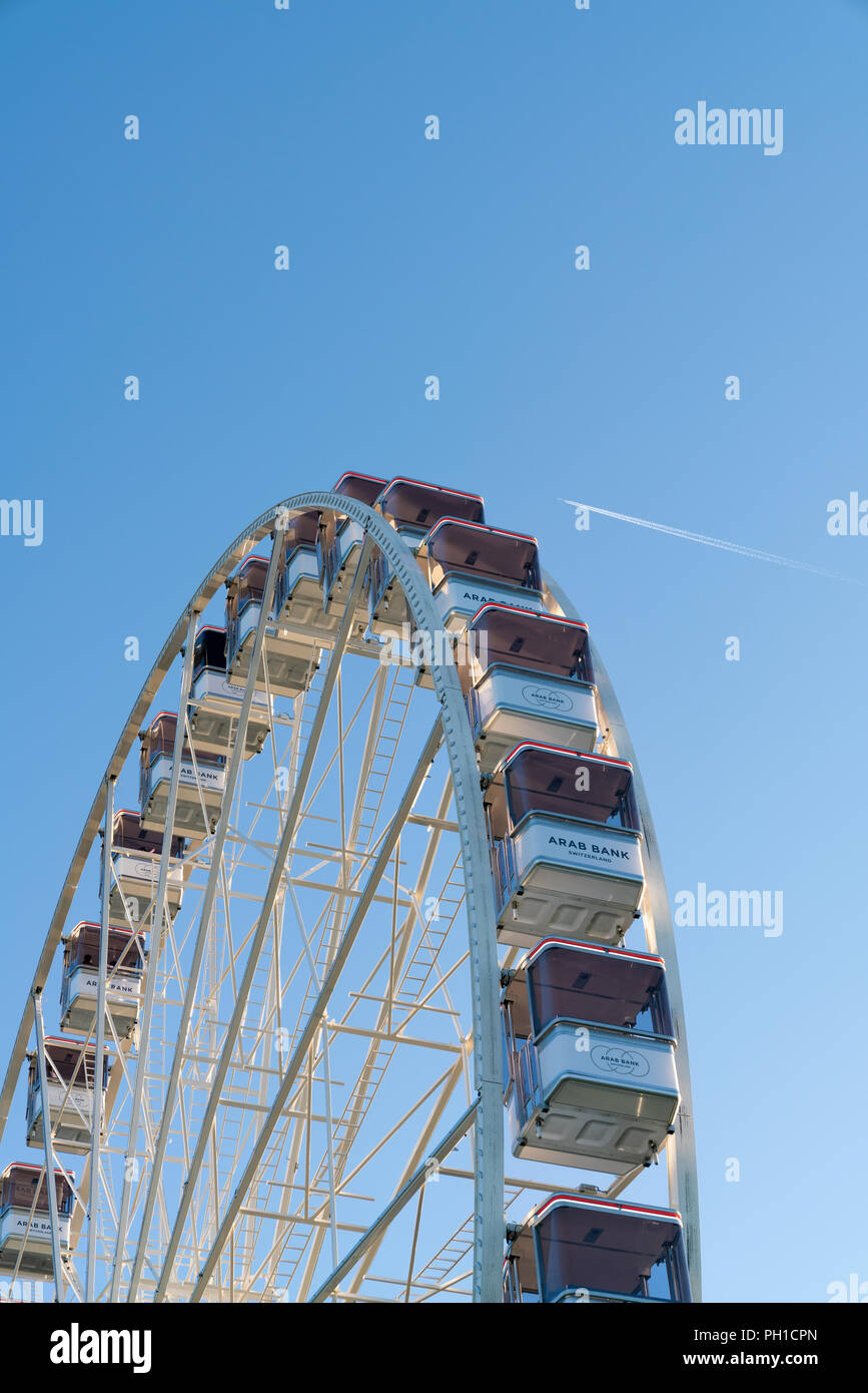 26. August 2018 - Genf, Schweiz. Vertikale Bild des Riesenrades Kabinen gegen den blauen Himmel und fliegenden Flugzeug. Stockfoto