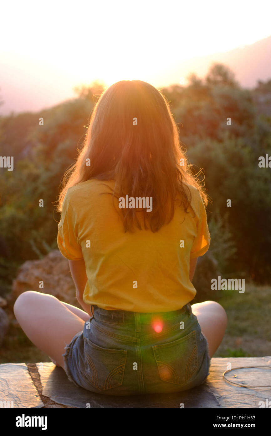 Jugendlich Mädchen im Schneidersitz beobachten ein Sonnenuntergang in den Bergen. Stockfoto