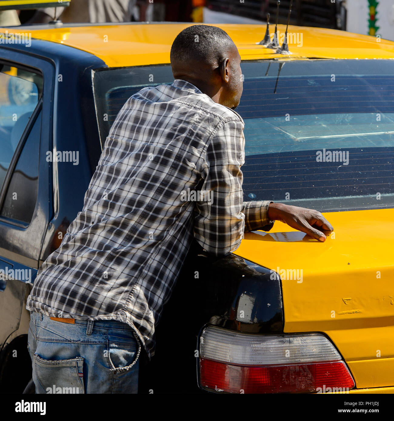 SAINT LOUIS, SENEGAL - Apr 24, 2017: Unbekannter senegalesischen Mann in Plaid Shirt lehnt sich an das Auto am lokalen Markt von Saint Louis, Senegal Stockfoto