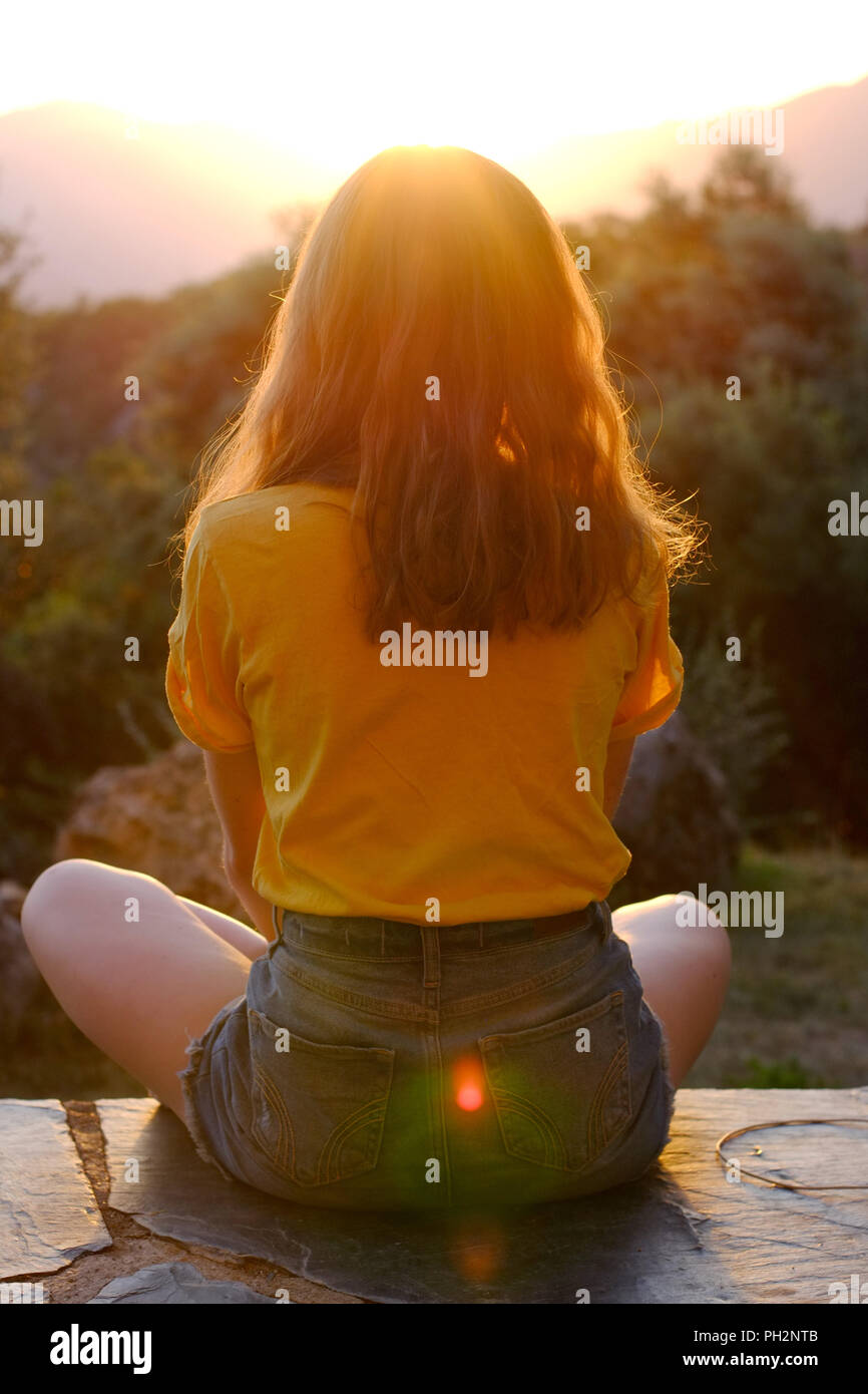 Jugendlich Mädchen im Schneidersitz beobachten ein Sonnenuntergang in den Bergen. Stockfoto