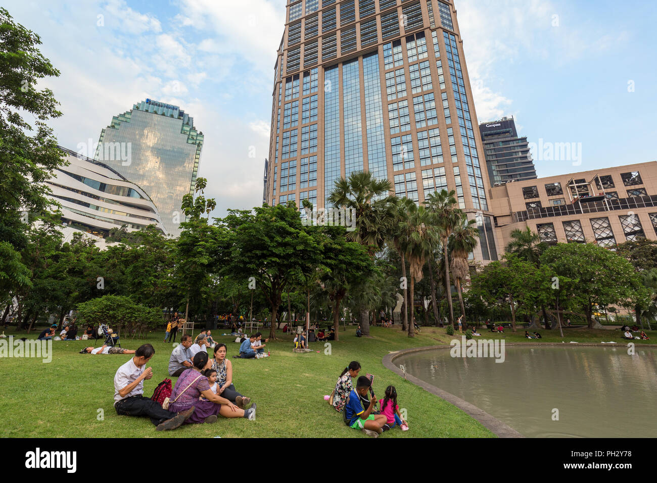 Blick auf einen Teich und viele Menschen in der Benchasiri Park und moderne Gebäude hinter dem Park in der Innenstadt von Bangkok, Thailand. Stockfoto