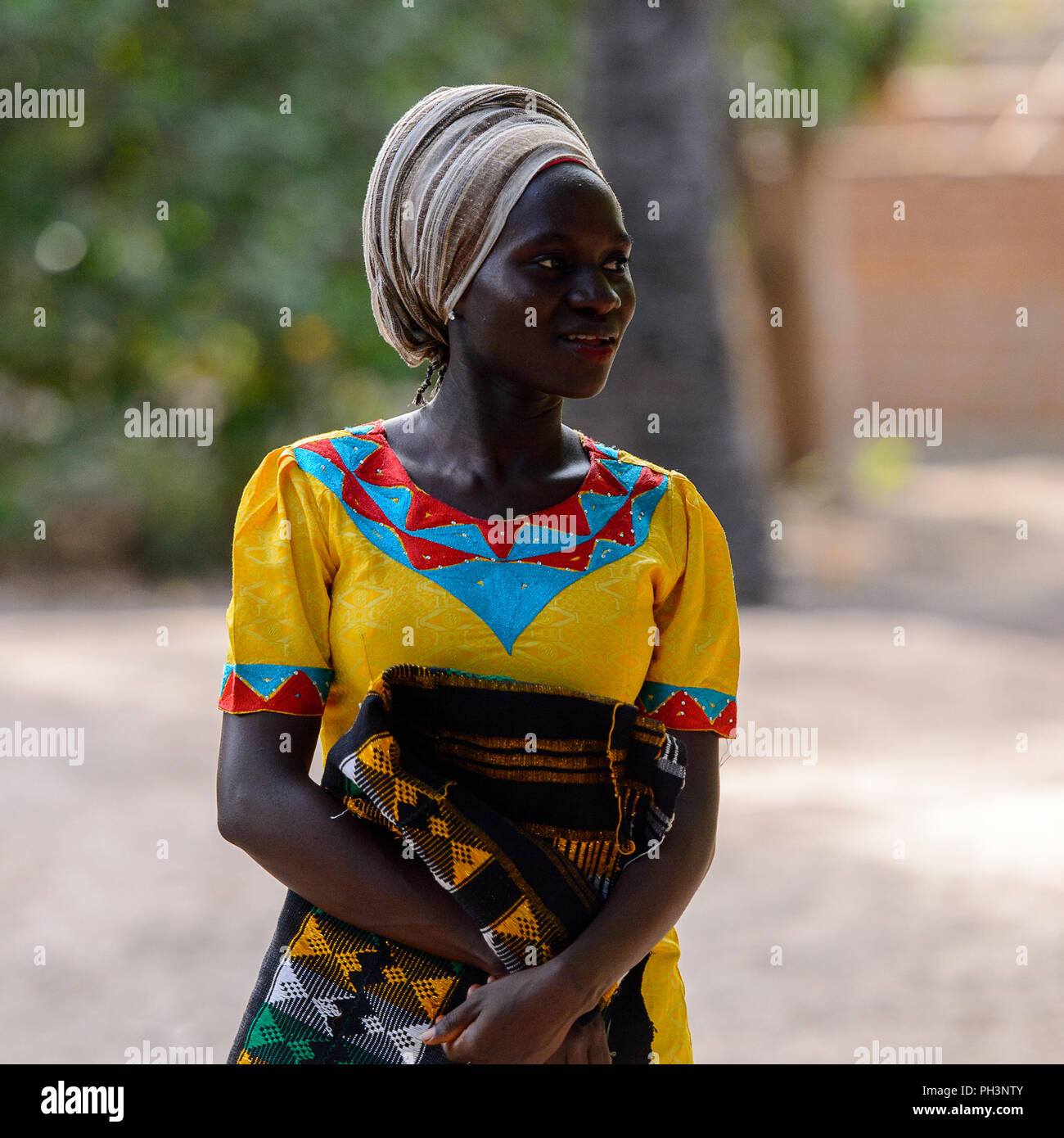 OUSSOUYE, SENEGAL - Apr 30, 2017: Unbekannter senegalesische Frau im gelben  Kleid und beige Kopftuch hält farbigen plaid im heiligen Wald in der Nähe  von Kag Stockfotografie - Alamy
