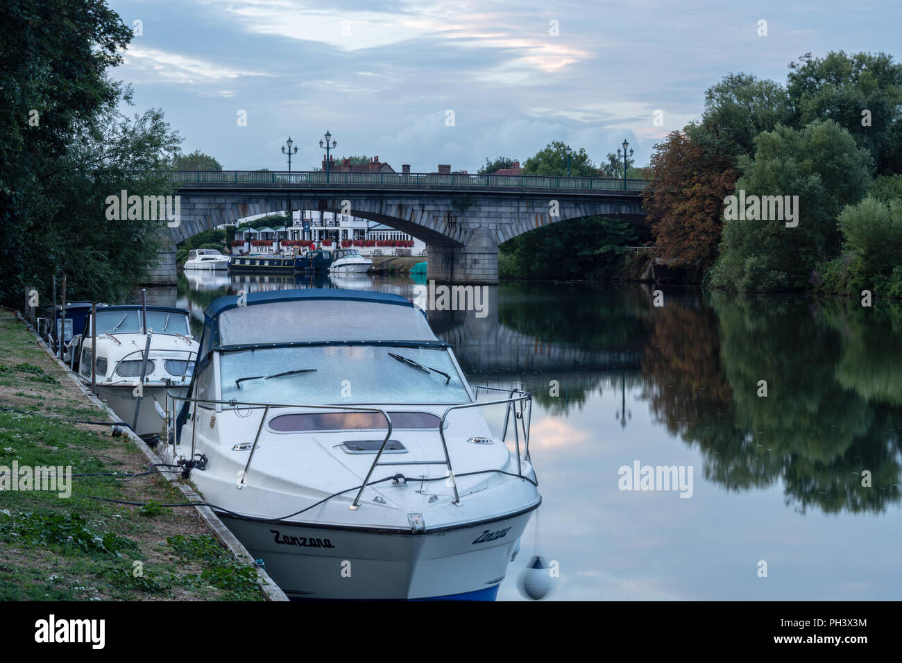 Boote am Ufer der Themse in Staines Brücke in der Morgendämmerung, Swan Hotel/Public House im Hintergrund Stockfoto