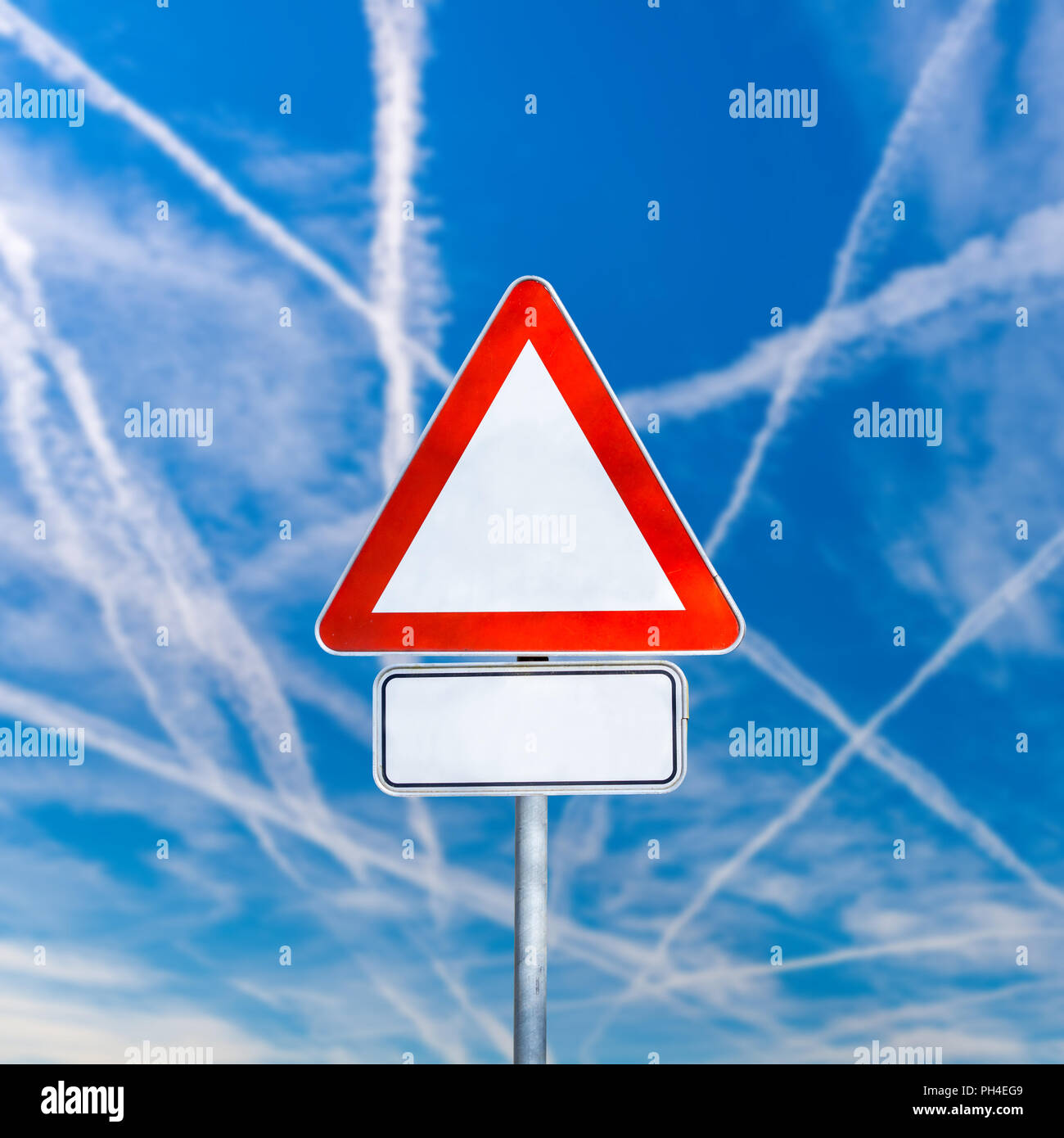 Leere weiße Dreieckverkehr Warnschild an einem Wegweiser gegen einen sonnigen blauen Himmel mit der Krise - Kreuzung Kondensstreifen von Jets mit Copyspace für Yo Stockfoto