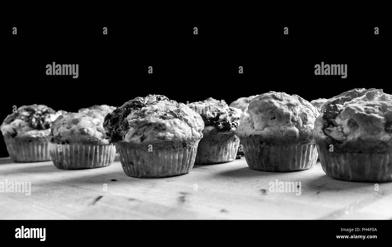 Schwarz-weiß Bild von einer Charge von frisch gebackene Muffins oder Cupcakes gegen einen dunklen Hintergrund mit Copyspace. Stockfoto