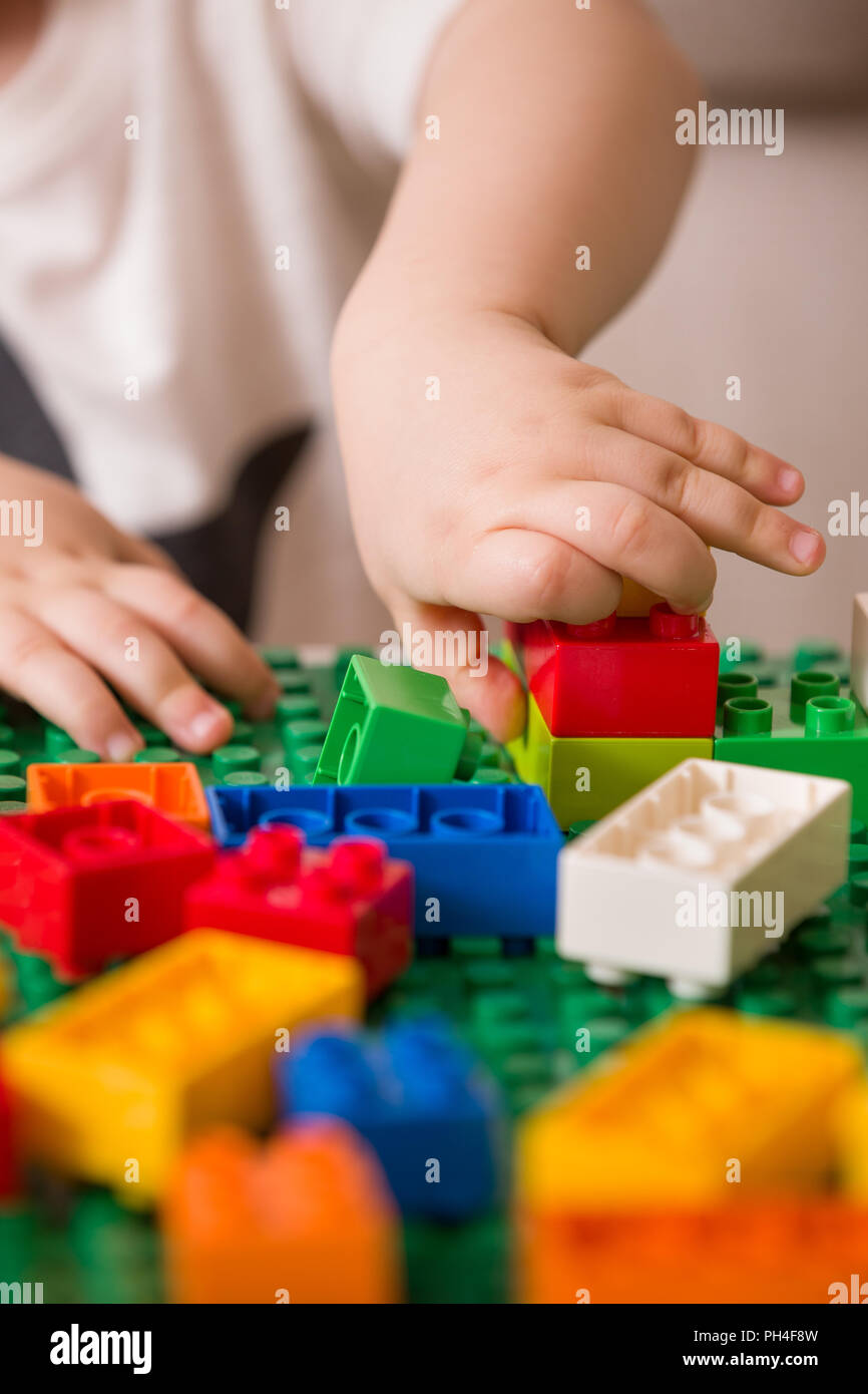 In der Nähe der Hände Kind spielen mit bunten Kunststoff Ziegel am Tisch. Kleinkind, das Spaß und Gebäude aus hellen Konstruktor Steine. Anfang l Stockfoto