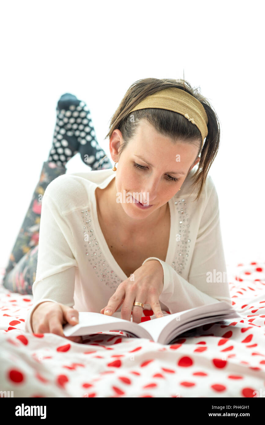 Attraktive Frau einen erholsamen Tag zu Hause liegen auf einem bunten red Polka Dot counterpane auf ihrem Bett und liest einen Roman. Stockfoto