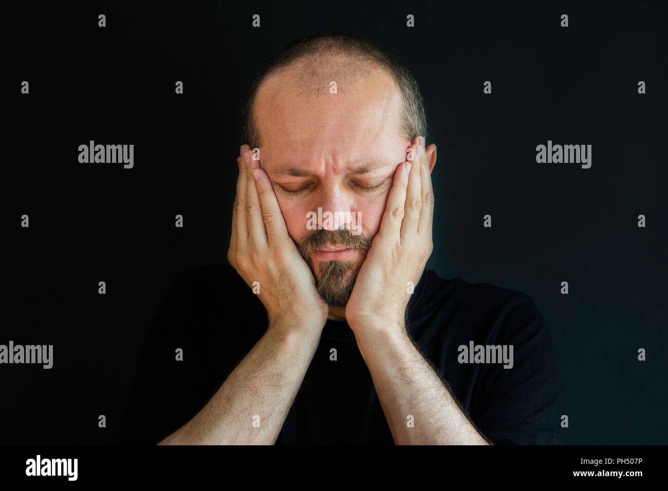 Ernster Mann mit Bart und Schnurrbart auf schwarzem Hintergrund in Low Key, Frustration und Verzweiflung Geste Stockfoto