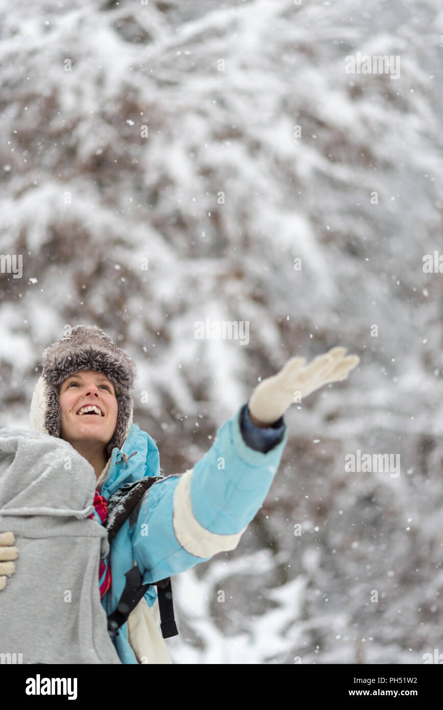 Herzlich Frau ihre Hand aus dem Schnee im Winter bei Schneefall, als sie einen Spaziergang in einem verschneiten Wald genießt gekleidet. Stockfoto
