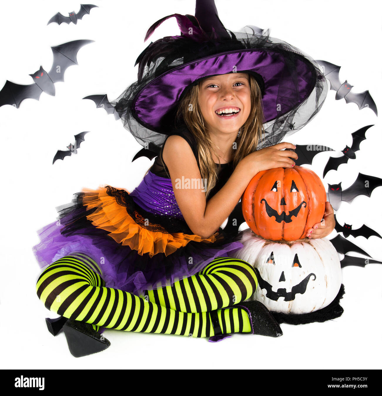 Happy Halloween Hexe & Glückliche Kürbis. Kleines Mädchen mit einem Halloween Kostüm einer Hexe mit Hut, gestreiften Beinen halten zwei smiley Halloween Kürbisse Stockfoto