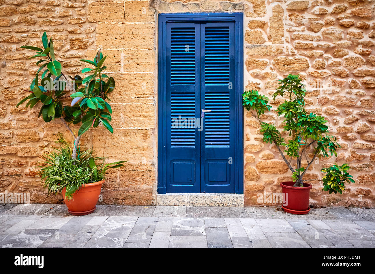 Alte Steinmauer mit blauer Tür und Blumentöpfe, Mallorca, Balearen, Spanien. Stockfoto