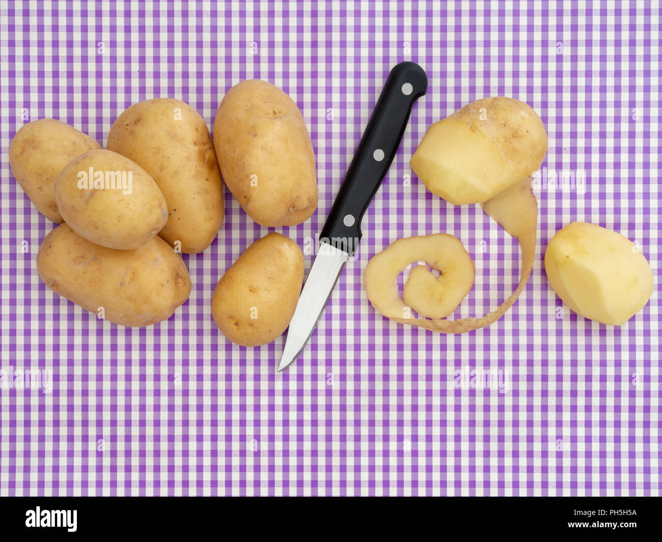 Zubereitung von Speisen, Schälen von Kartoffeln auf den Purple gingham Oberfläche. Mit Messer, Ansicht von oben mit Copyspace. Retro Design. Stockfoto