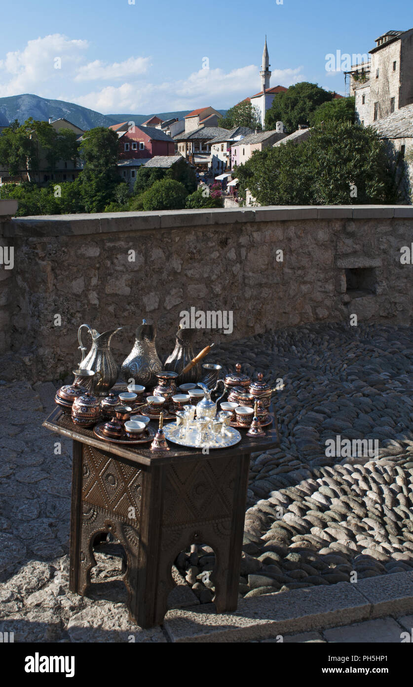 Bosnien: Eine kleine Tabelle mit typischen Kupfer Tee und Kaffee setzt zum Verkauf und Blick auf die Skyline der Stadt Mostar mit der Koski Mehmed Pascha Moschee Stockfoto