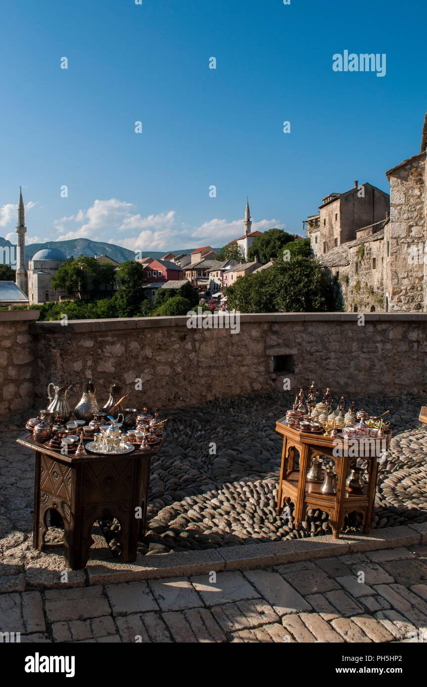 Bosnien: Eine kleine Tabelle mit typischen Kupfer Tee und Kaffee setzt zum Verkauf und Blick auf die Skyline der Stadt Mostar mit der Koski Mehmed Pascha Moschee Stockfoto