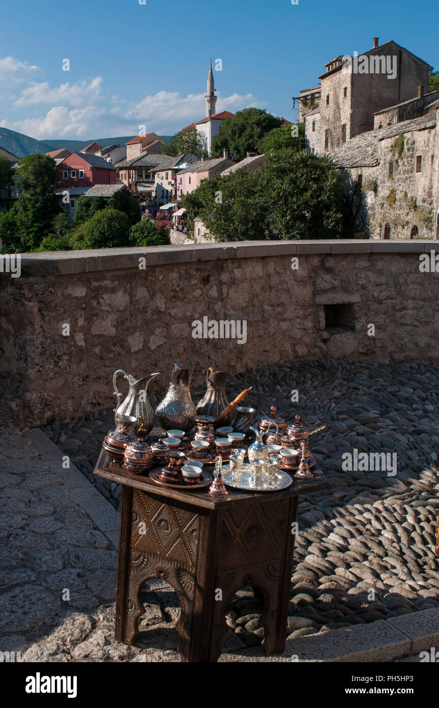 Bosnien: Eine kleine Tabelle mit typischen Kupfer Tee und Kaffee setzt zum Verkauf und Blick auf die Skyline der Stadt Mostar mit der Koski Mehmed Pascha Moschee Stockfoto
