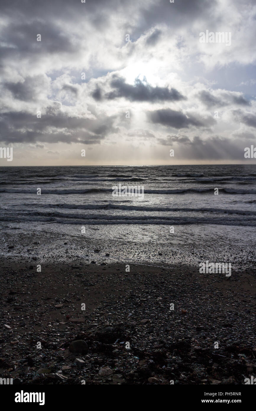 Sonnenlicht, das durch die Wolken über dem Meer gegen einen felsigen Ufer plätschern, St. Johns Point, County Down, Nordirland. (vertikal) Stockfoto