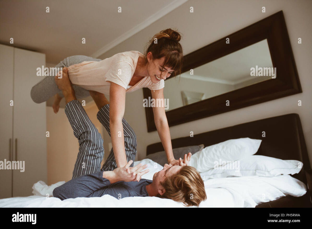 Glückliches Paar im Bett spielen und Spaß haben. Man liegt auf dem Bett und seine Frau heben mit seinen Füßen halten ihre Hände. Stockfoto