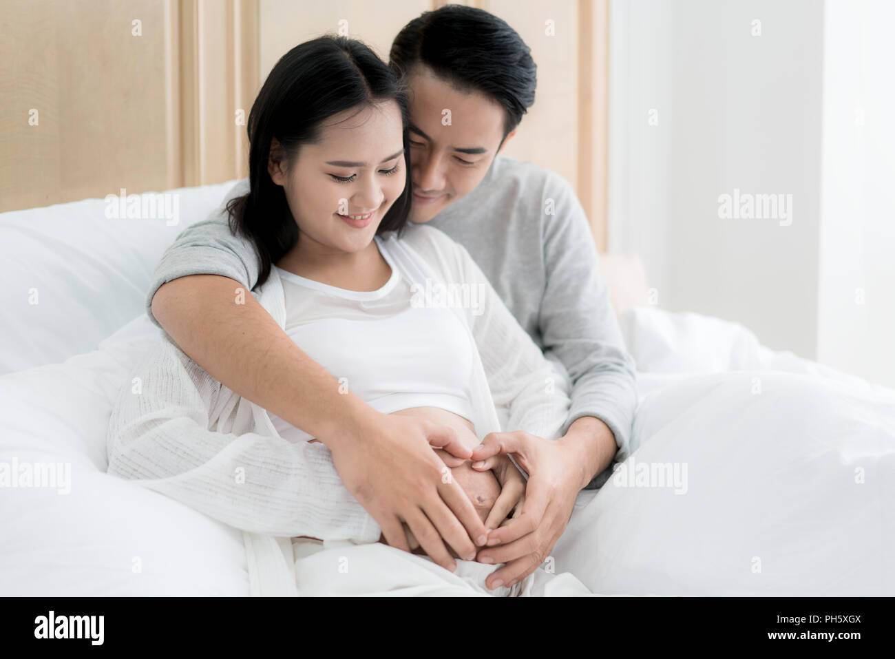 Zugeschnittenes Bild der schönen schwangeren Frau und ihrem stattlichen Mann umarmen den Bauch. Liebe Paar Hände machen ein Herz auf den schwangeren Bauch. Stockfoto