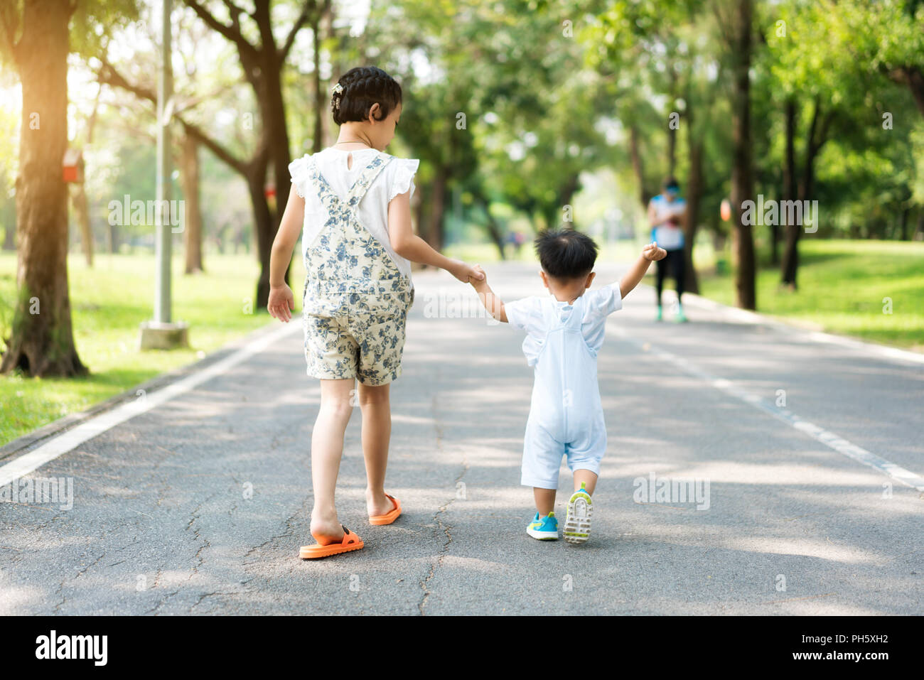 Asiatische Schwester halten Hände mit kleinen Kindern zu Fuß auf der Straße, im Park mit Sonnenstrahlen. Stockfoto