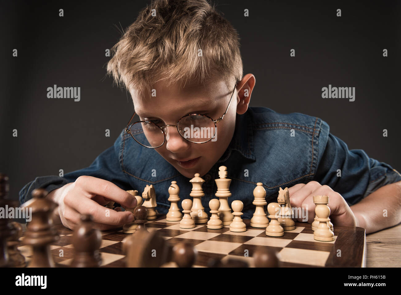 Im Mittelpunkt kleiner Junge in Brillen Schach spielen am Tisch auf grauem Hintergrund Stockfoto