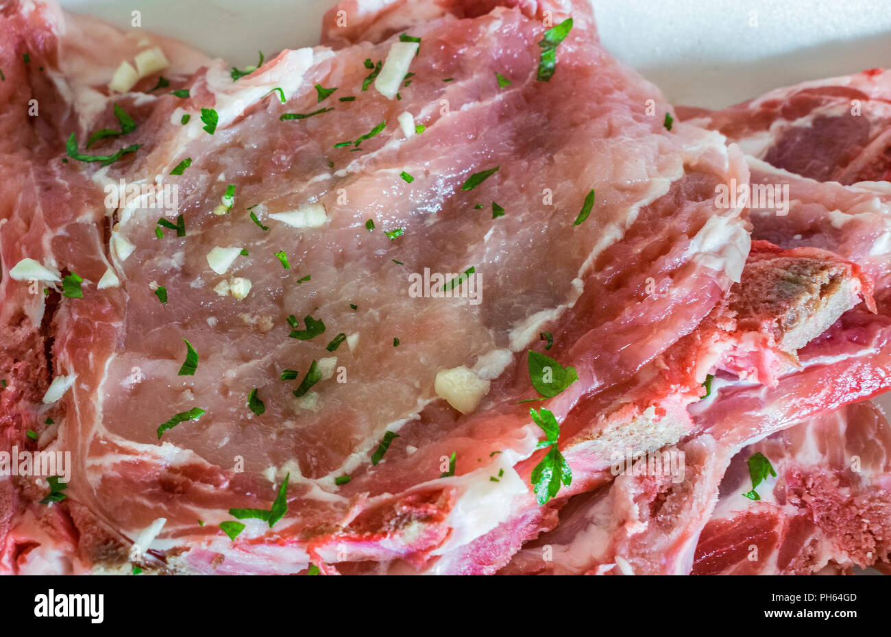 Raw Schweinekoteletts mit kleinen Stücken von Knoblauch und Petersilie Stockfoto