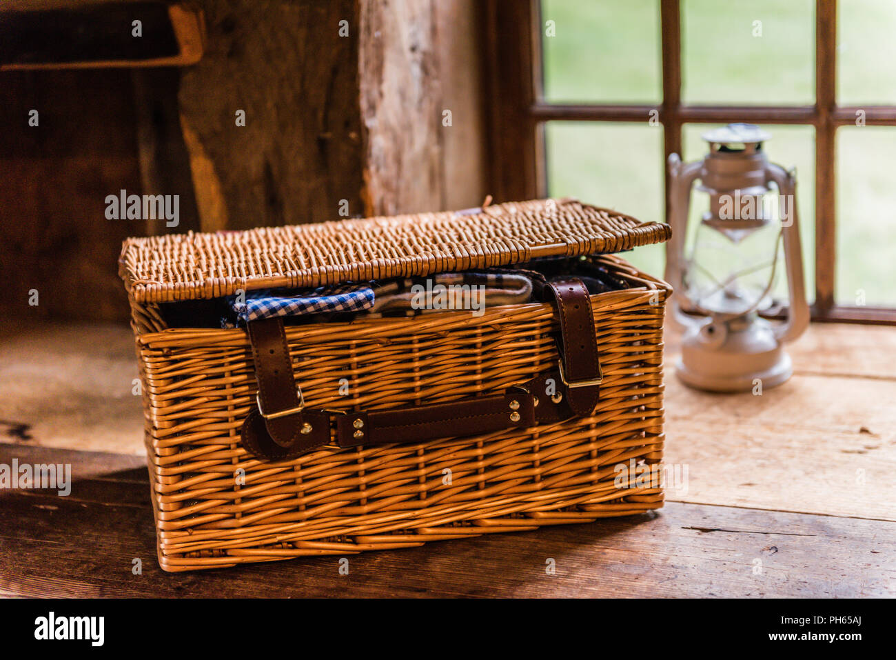 Ein rattan Picknickkorb sitzt auf Holz Sitzbank, mit blauen ginham Serviette peeking Out. Stockfoto