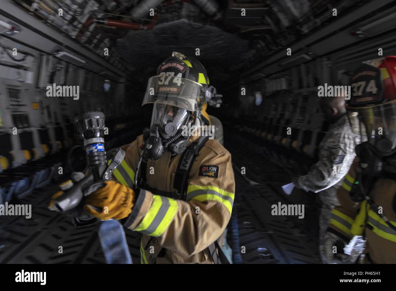 Senior Airman Tianna Cooper, 374 zivilen Engieer Squadron Feuerwehrmann, führt den ersten Eintrag eines simulierten Vater an Bord einer C-17 Globemaster III während ein Notfallplan Übung in Yokota Air Base, Japan, 25. Juni 2018. Flieger von der 730th Air Mobility Squadron und 374 CES Feuerwehr führte eine simulierte Feuer an Bord einer C-17 und Einarbeitung Training. Stockfoto