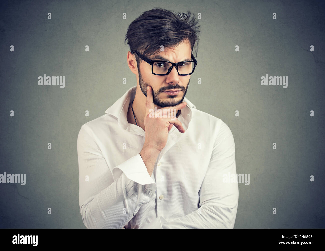 Hübscher junger Mann mit Bart in Brillen suchen zweifelhaft und neugierig auf grauem Hintergrund Stockfoto