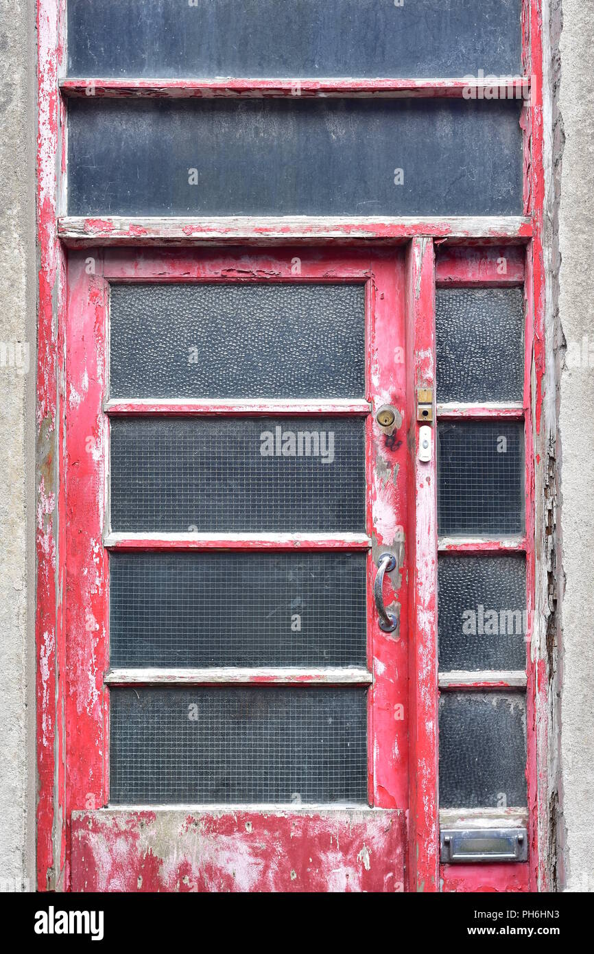 Verwitterten hölzernen Tür rot lackiert mit Metallgriff und Messing. Fensterscheiben haben drahtgitter zum Schutz. Stockfoto