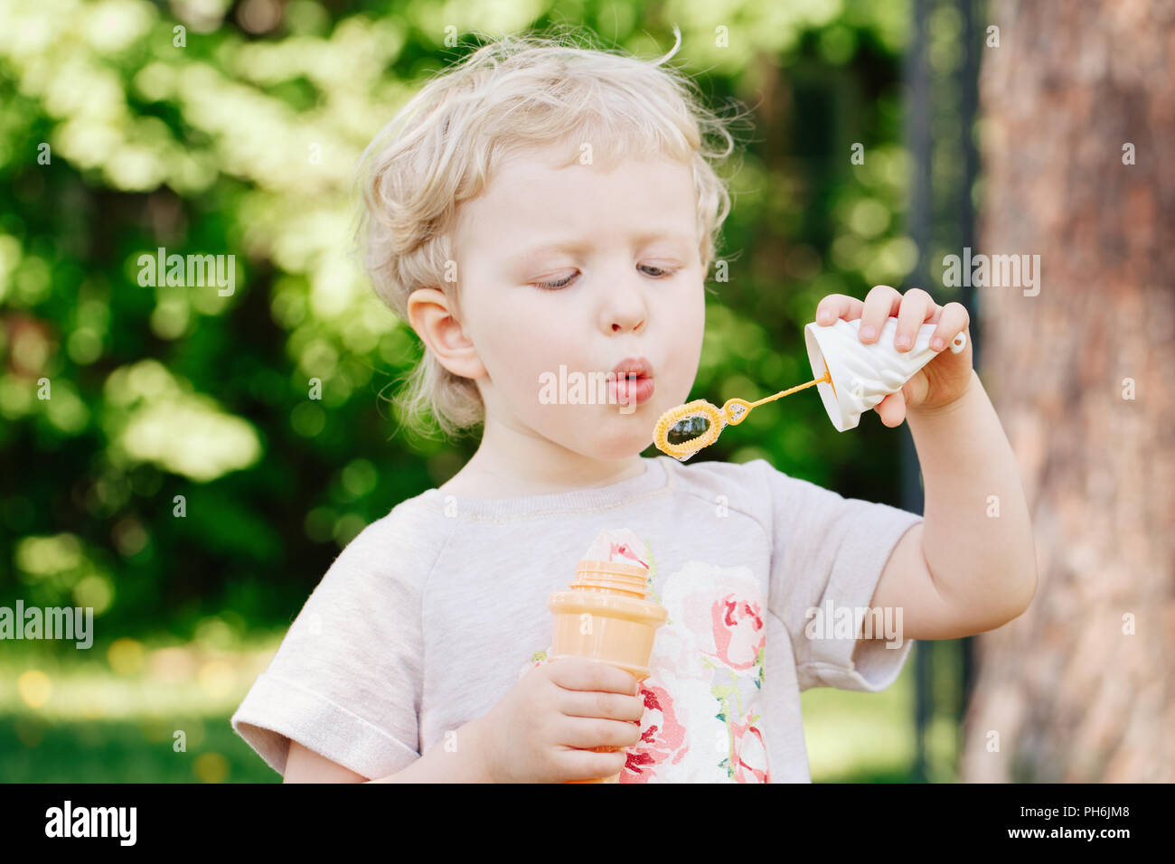 Portrait von niedlichen Lustige kleine blonde Kaukasier Kind girl Toddler, stehen im grünen Wald Feld Wiese bläst Seifenblasen, hellen Sommertag, su Stockfoto