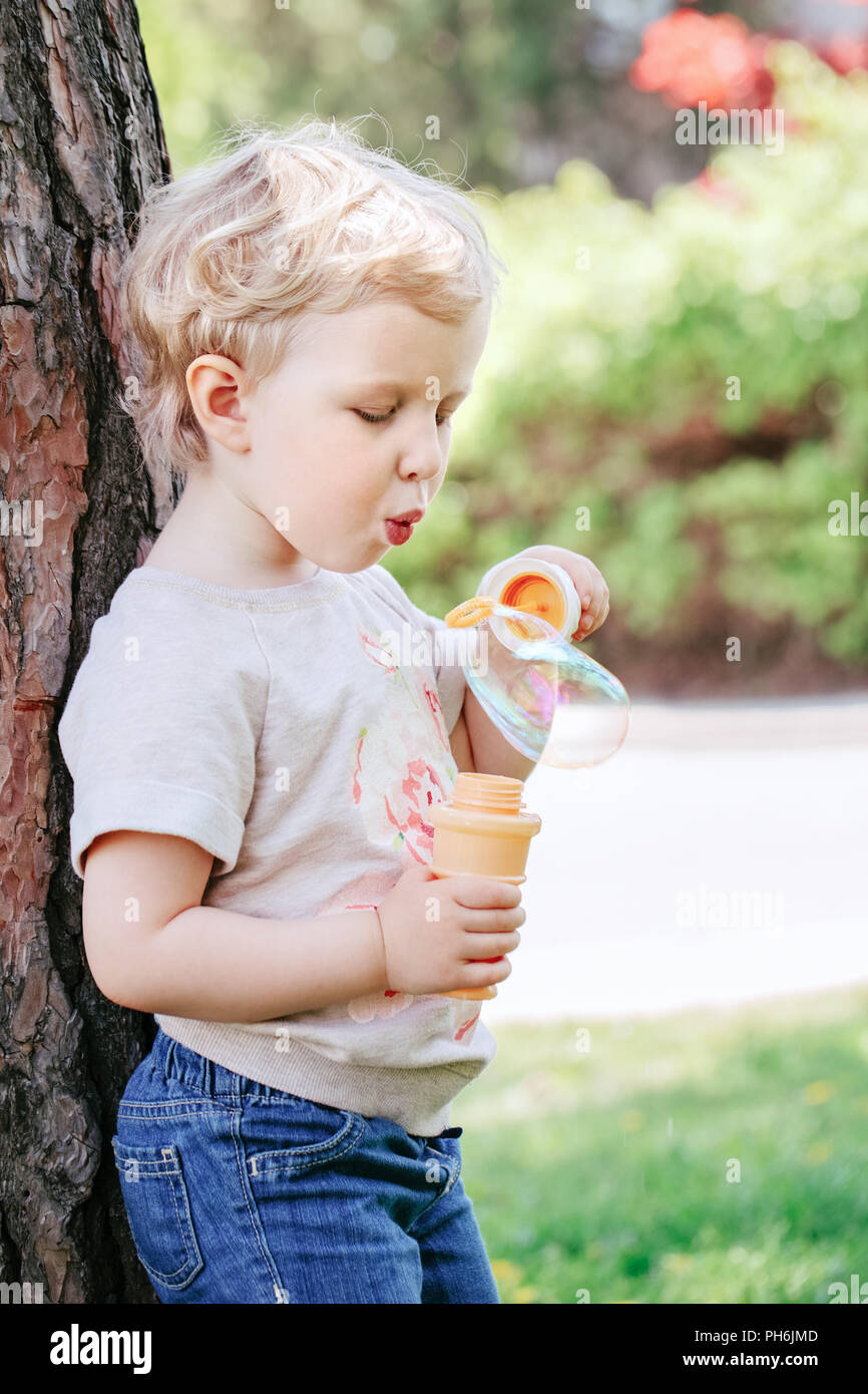 Portrait von niedlichen Lustige kleine blonde Kaukasier Kind girl Toddler, stehen im grünen Wald Feld Wiese bläst Seifenblasen, hellen Sommertag, su Stockfoto