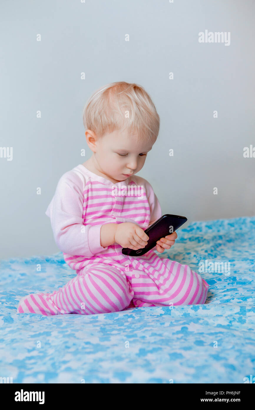 Cute adorable white Kaukasischen blond Baby einen Anruf machen, Spielen mit Handy mit lustigen Gesichtsausdruck, Lifestyle neue Generation Technol Stockfoto