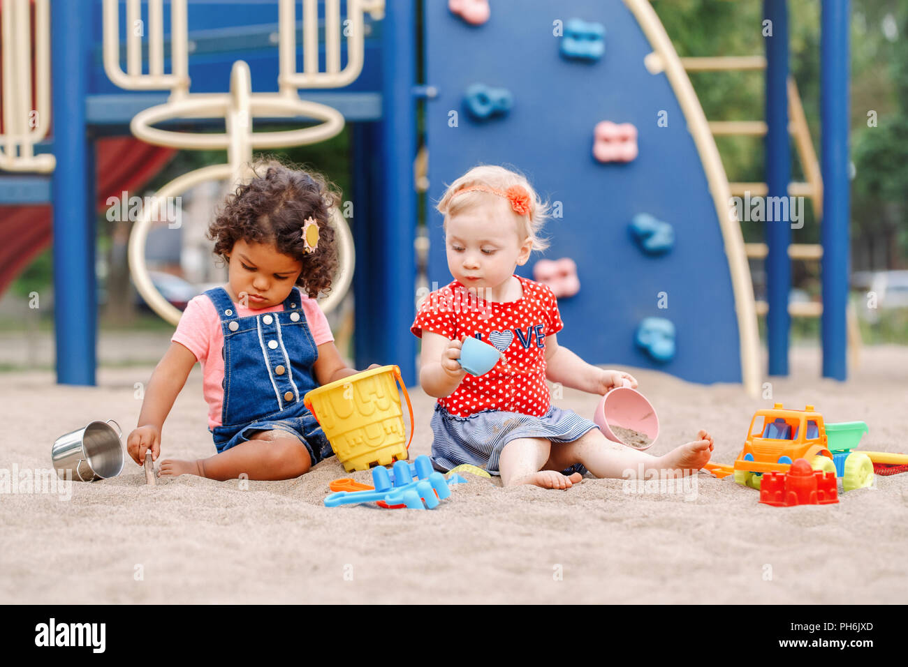 Interessierte schauen. Zwei süße Kaukasischen und hispanische Latein Babys Kinder sitzen im Sandkasten spielen mit Kunststoff farbenfrohen Spielzeuge. Kleine Mädchen Freunde hav Stockfoto