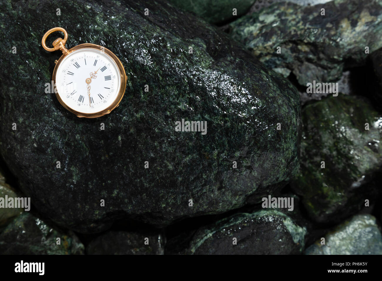 Nahaufnahme von einem schönen Classic Gold Taschenuhr Festlegung auf nassen grüne Steine Stockfoto